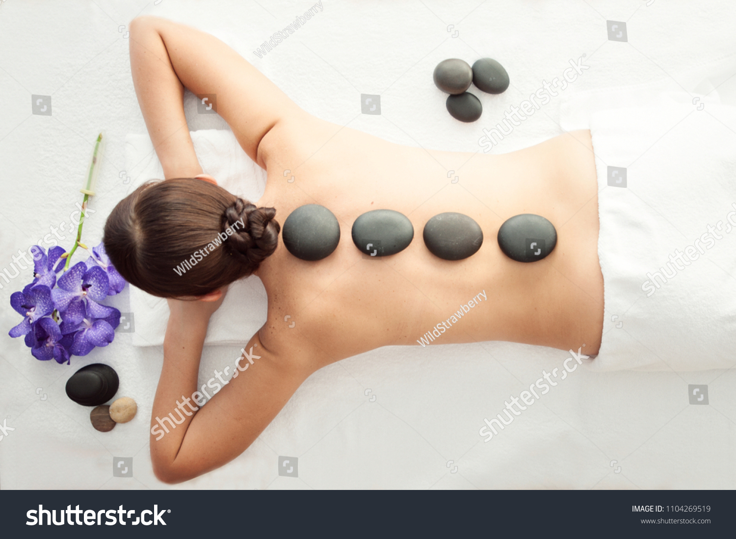Stone treatment. Top view of beautiful young woman lying on front with spa stones on her back.  Beauty treatment concept. #1104269519