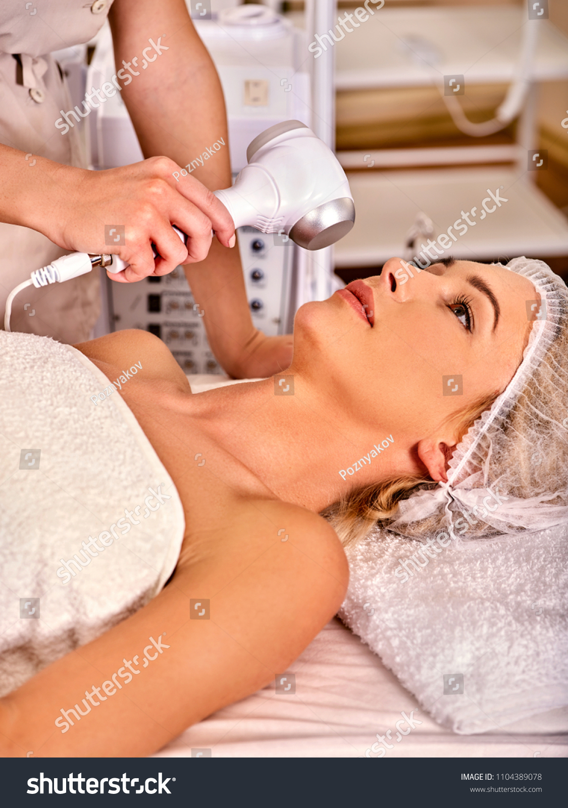 Ultrasonic facial treatment on ultrasound face machine. Woman receiving electric lift massage at spa salon. Electronic stimulation female muscles microcurrent therapy. Removal of pigmented spots. #1104389078