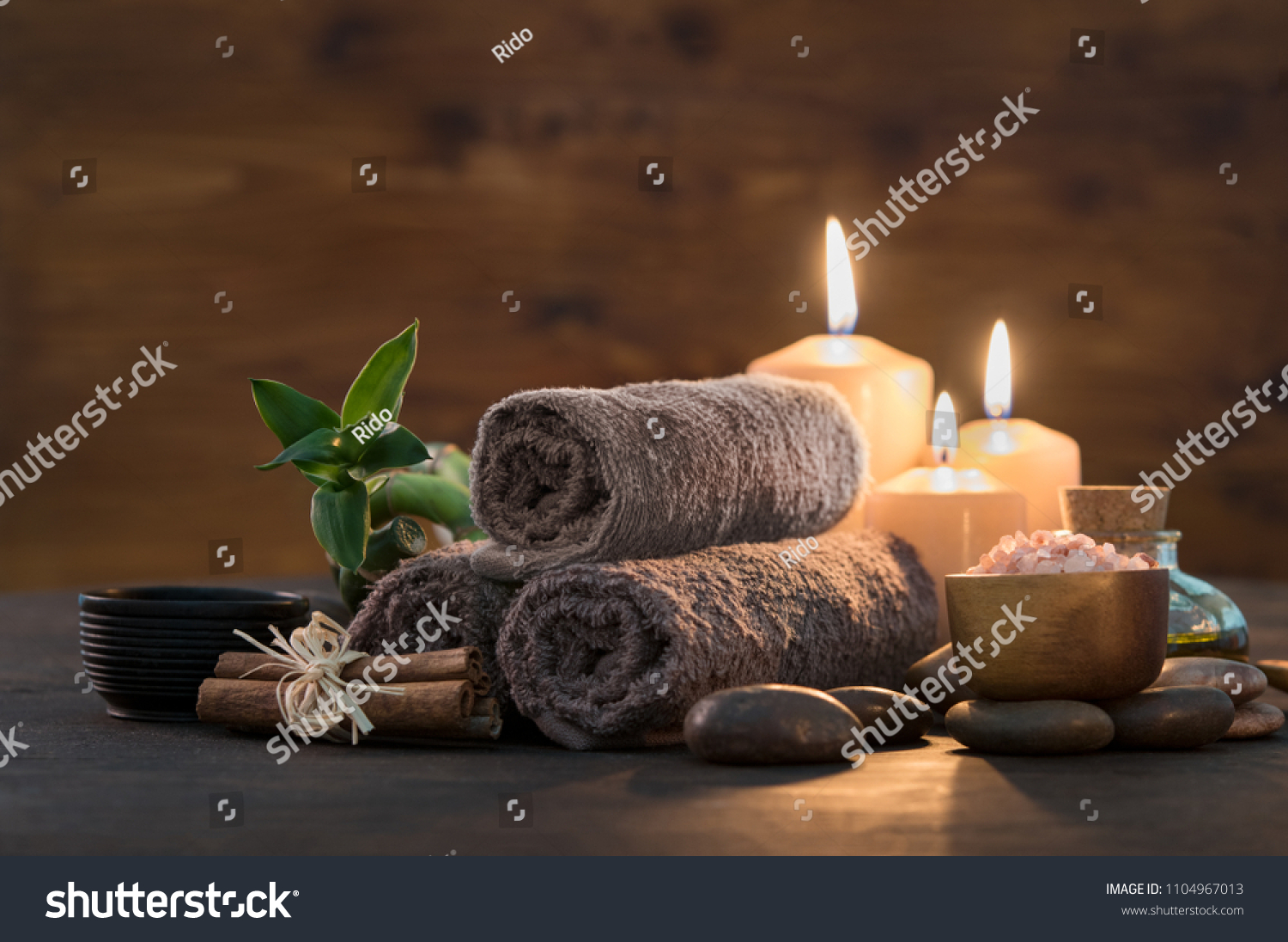 Brown towels with bamboo and candles for relax spa massage and body treatment. Composition with candles, spa stones and salt on wooden background. Spa and wellness setting ready for beauty treatment.  #1104967013