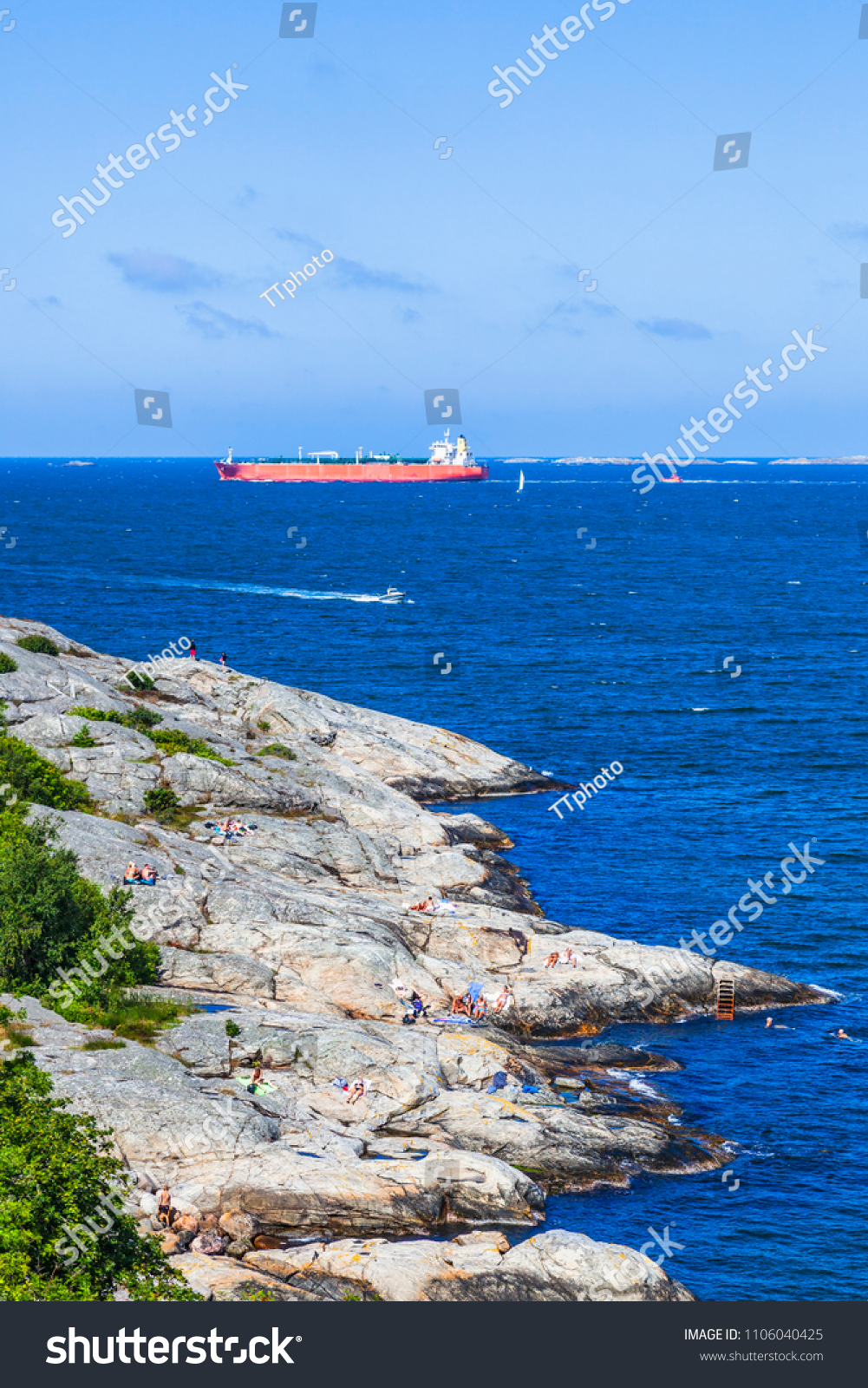 Rocky coast with sunbathing people and a cargo ship on the sea #1106040425