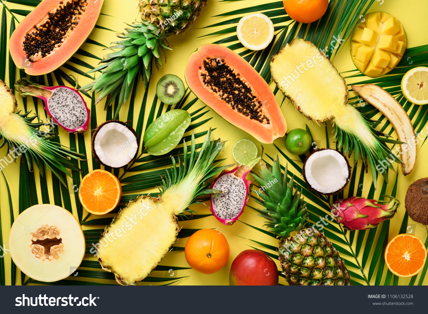 Exotic fruits and tropical palm leaves on pastel yellow background - papaya, mango, pineapple, banana, carambola, dragon fruit, kiwi, lemon, orange, melon, coconut, lime. Top view