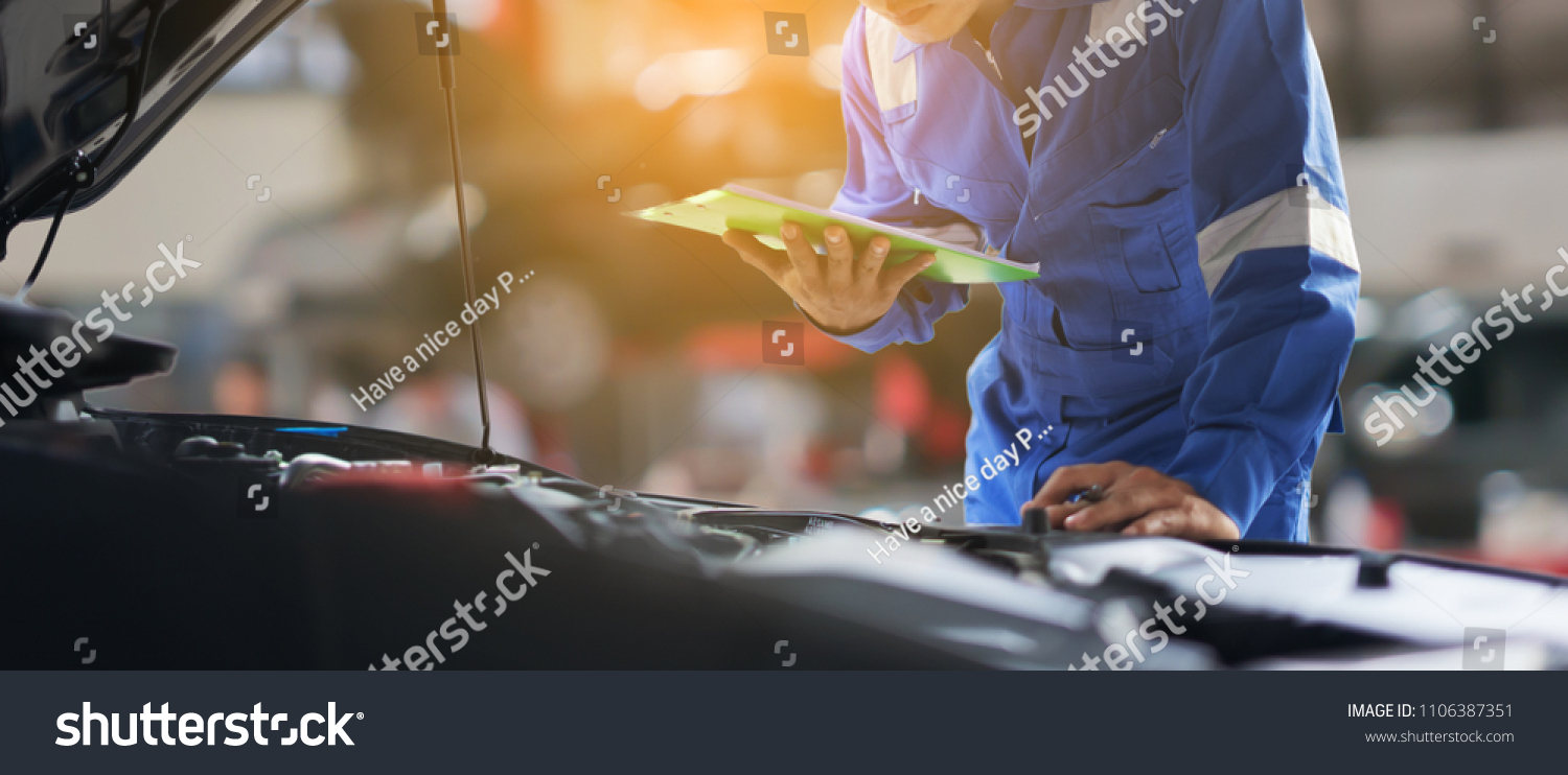 car service, repair, maintenance concept - Asian auto mechanic man or Smith writing to the clipboard at workshop warehouse, technician doing the checklist for repair machine a car in the garage,banner #1106387351