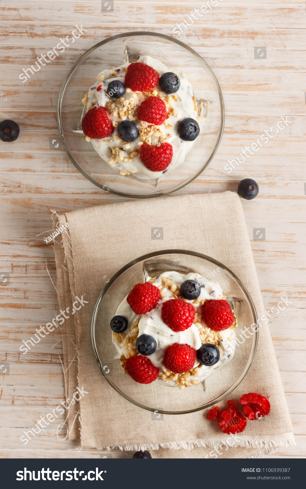 Raspberries, blueberries, cereals and yogurt in a glass bowl on sackcloth and wooden slats. Healthy breakfast for a healthy life. Vertical image view from above. #1106939387