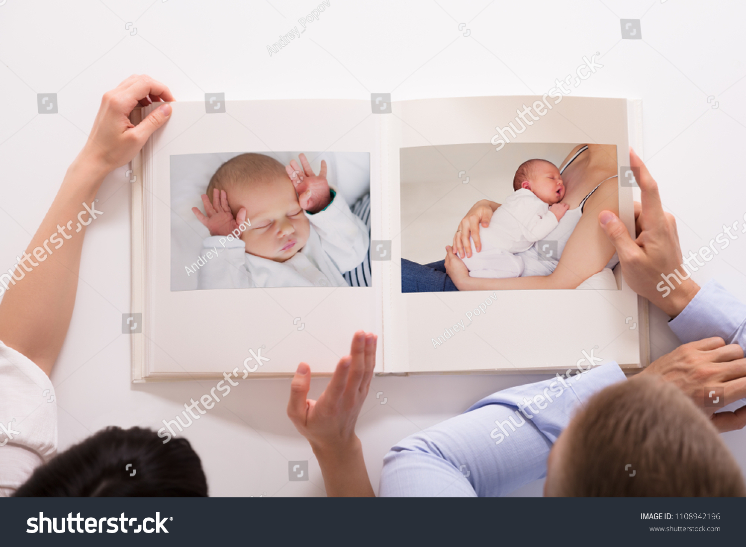 Elevated View Of Couple Looking At Baby's Photo Album On White Background #1108942196