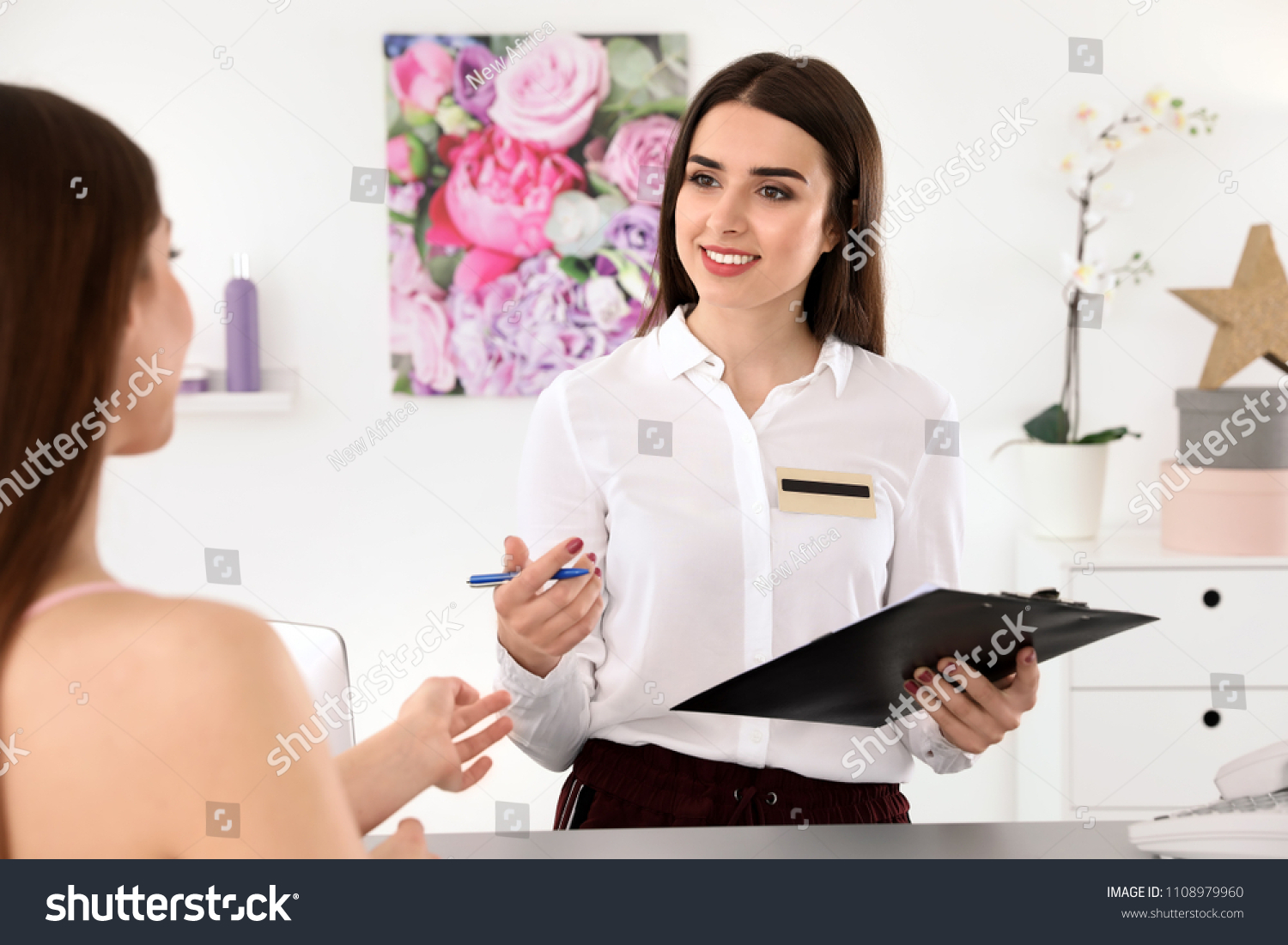 Young receptionist working with client at desk in beauty salon #1108979960