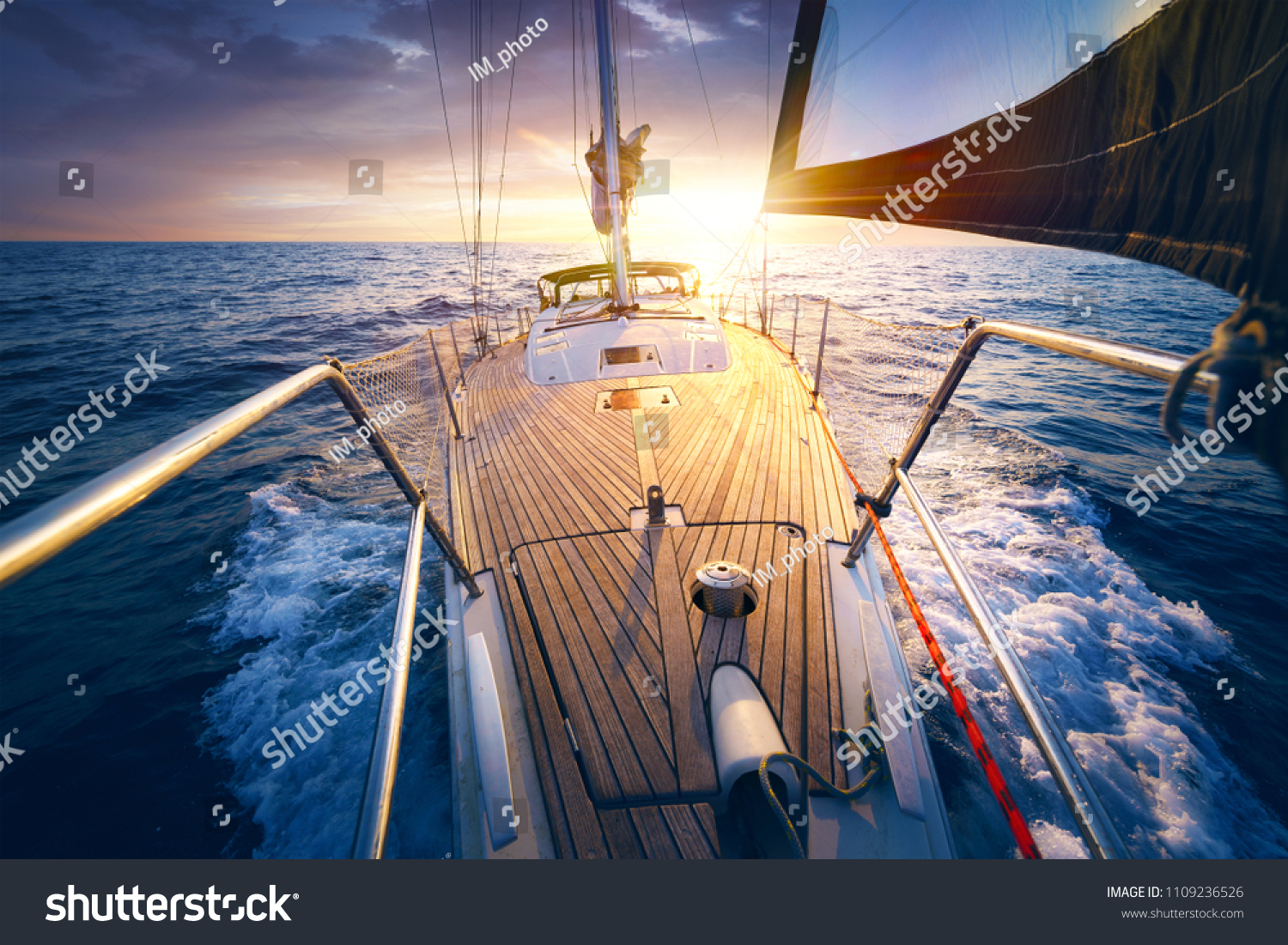 Sunset at the Sailboat deck while cruising / sailing at opened sea. Yacht with full sails up at the end of windy day. Sailing theme - background. #1109236526