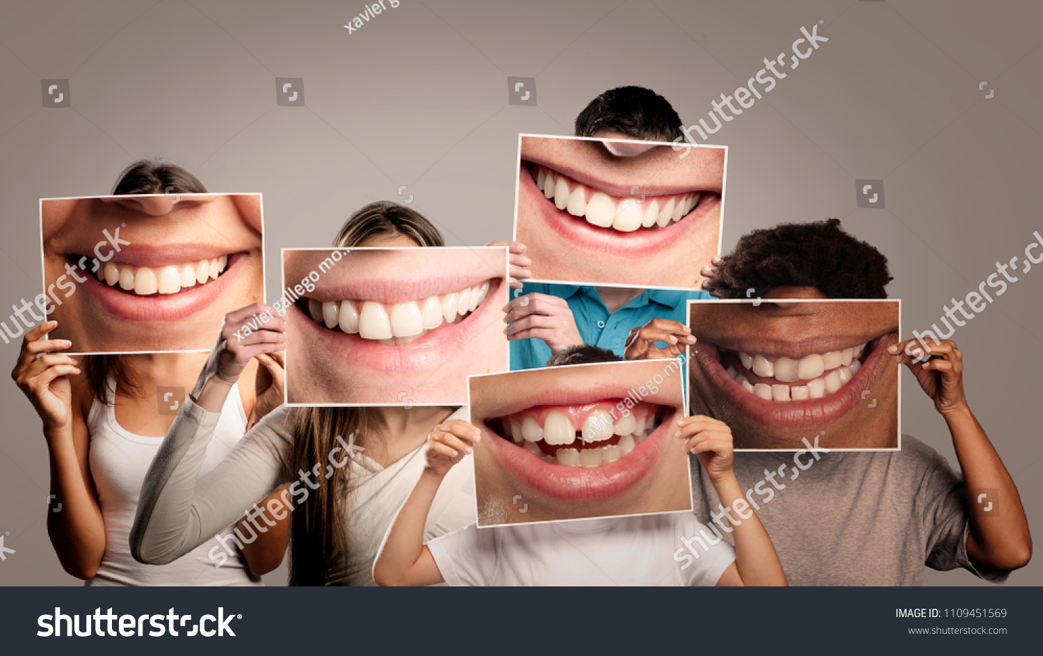group of happy people holding a picture of a mouth smiling on a gray background #1109451569