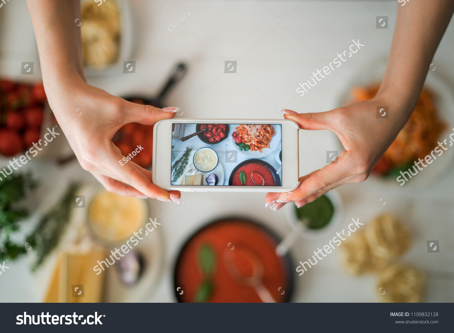 Hands with the smart phone pictures of meal. Young woman, cooking blogger is cooking at the home kitchen in sunny day and is making photo at smartphone. Instagram food blogger workshop concept. #1109832128