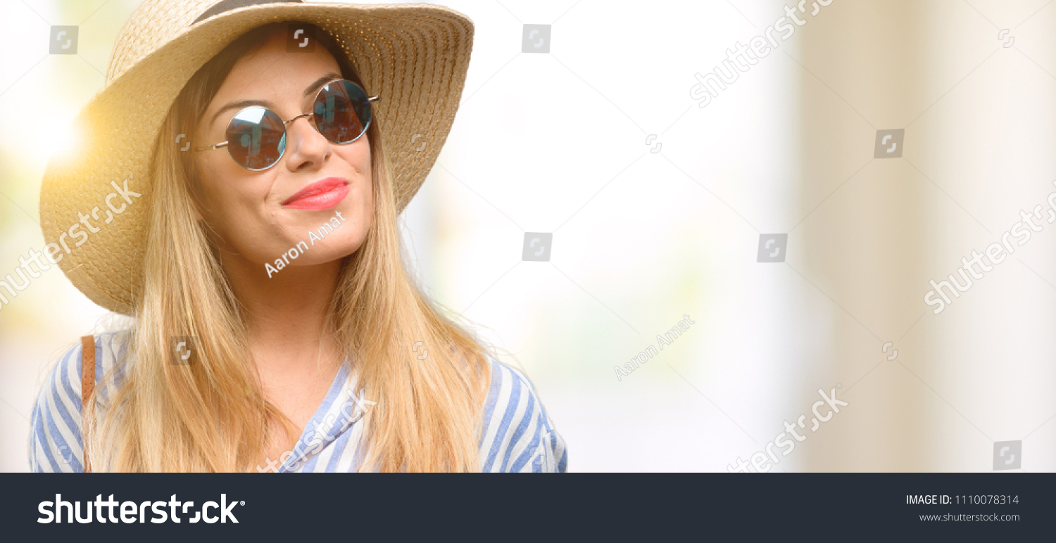 Young woman wearing sunglasses and summer hat holding blank advertising banner, good poster for ad, offer or announcement, big paper billboard #1110078314