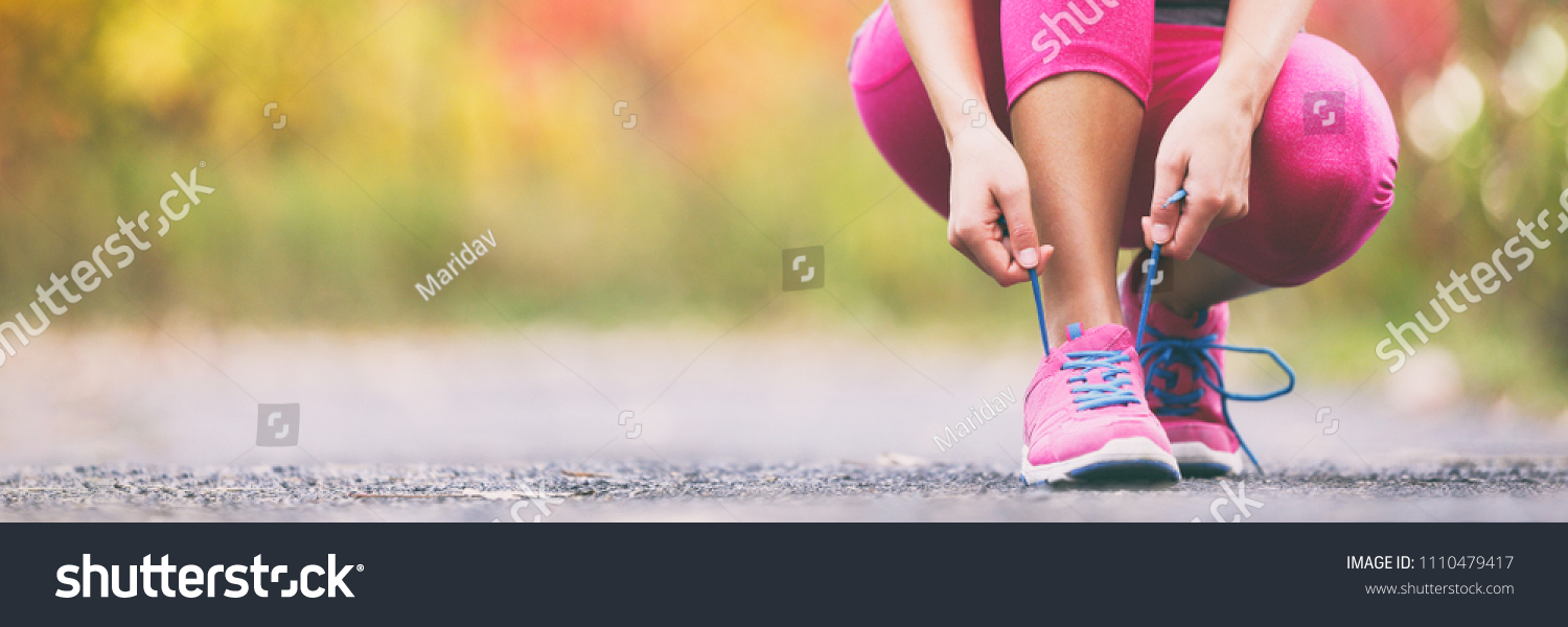 Running shoes runner woman tying laces for autumn run in forest park panoramic banner copy space. Jogging girl exercise motivation heatlh and fitness. #1110479417