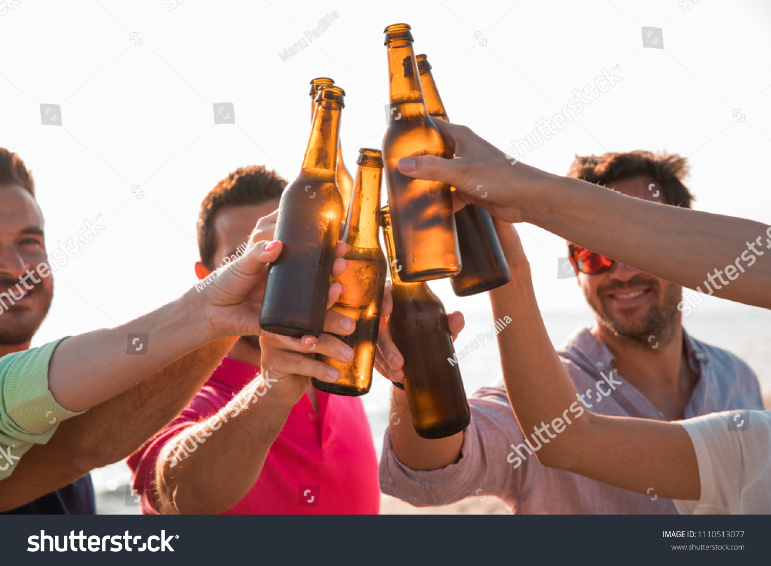 Cheers! Group of happy young people are toasting with bottles of beer in the beach. Celebration concept  #1110513077