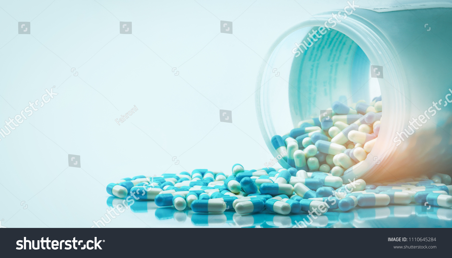 Blue and white capsules pill spilled out from white plastic bottle container. Global healthcare concept. Antibiotics drug resistance. Antimicrobial capsule pills. Pharmaceutical industry. Pharmacy. #1110645284