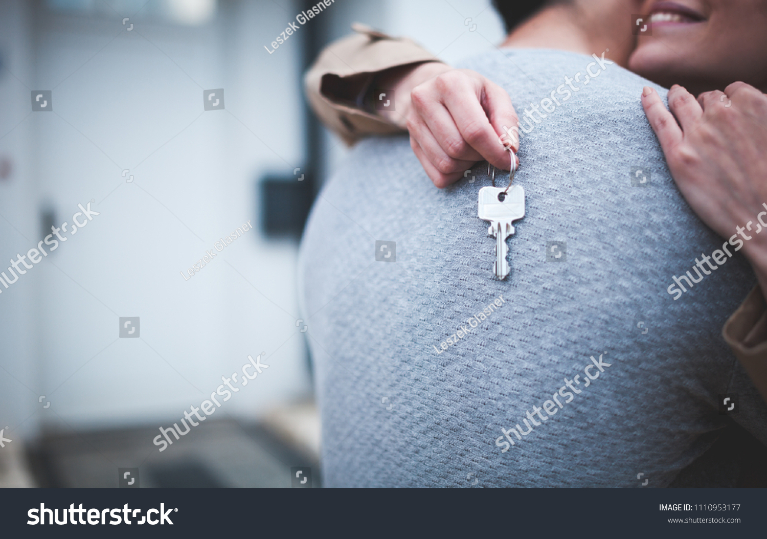 Young woman holding keys hugging husband in front of their new home after buying real estate #1110953177