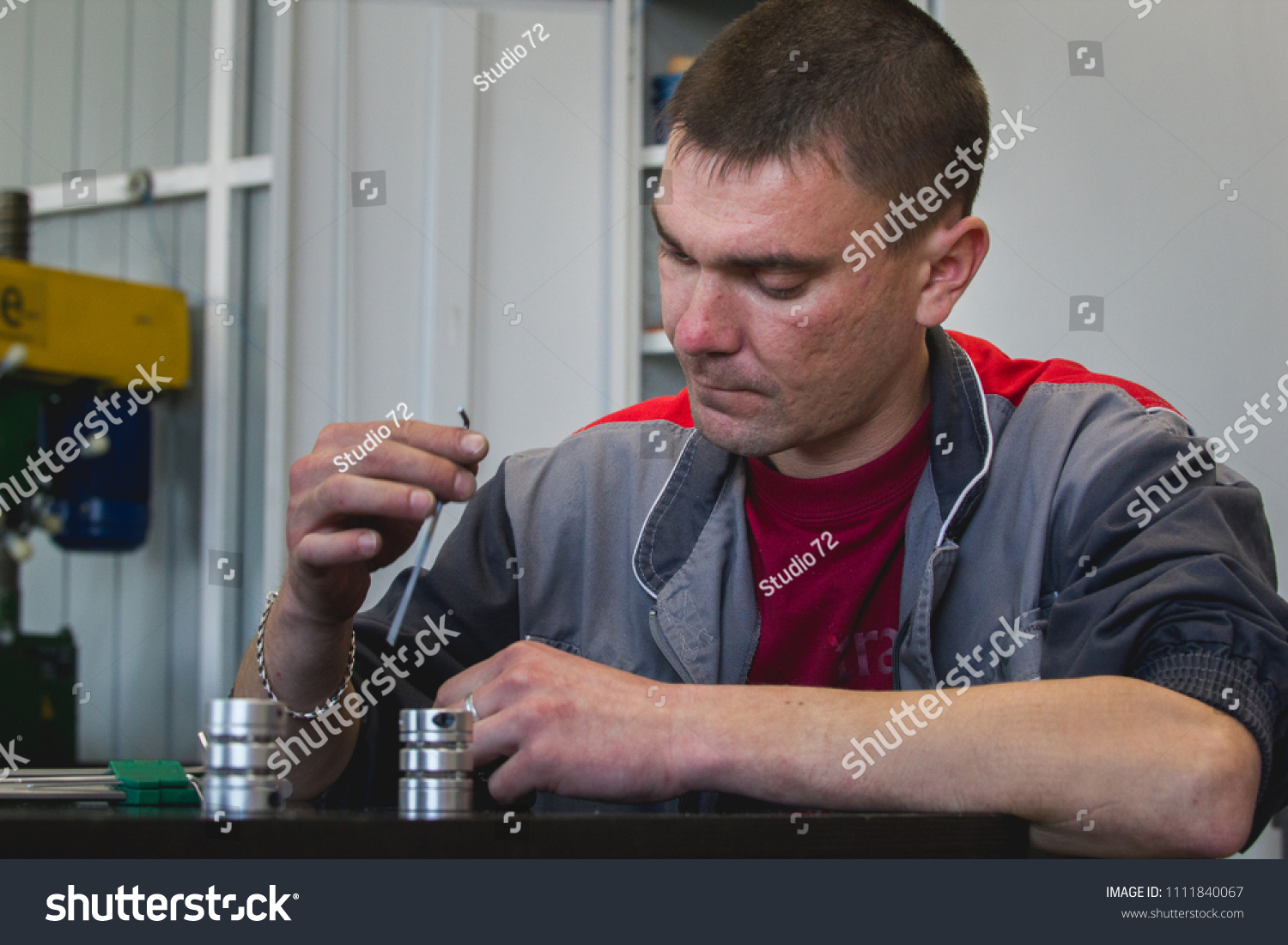 Male worker manually assembles metal detail for CNC machine at factory with lathes #1111840067
