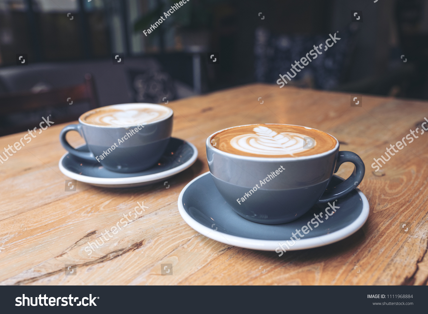Closeup image of two blue cups of hot latte coffee on vintage wooden table in cafe #1111968884