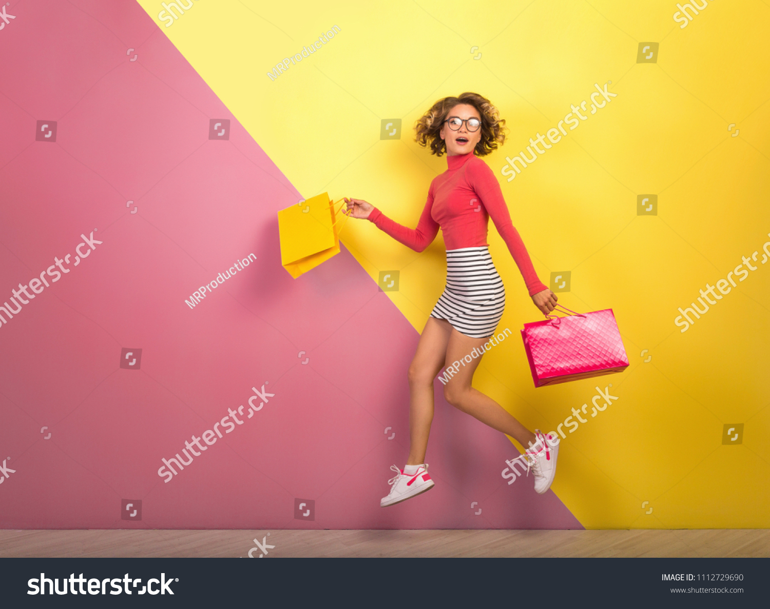 smiling attractive woman, stylish colorful outfit jumping with shopping bags, happy, pink yellow background, polo neck, striped mini skirt, sale, discount, shopaholic, fashion summer trend, emotional #1112729690