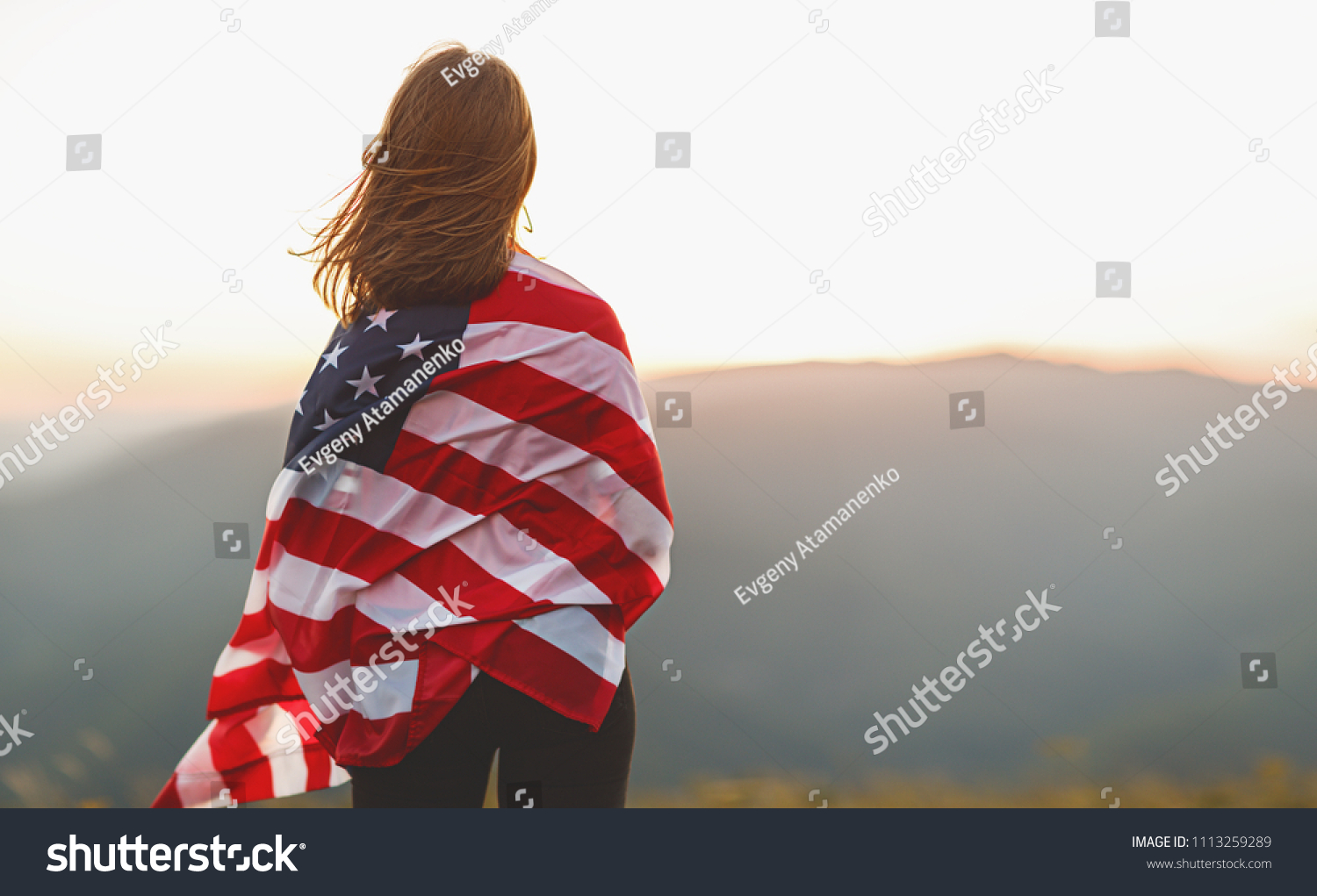 young happy woman with flag of united states enjoying the sunset on nature #1113259289
