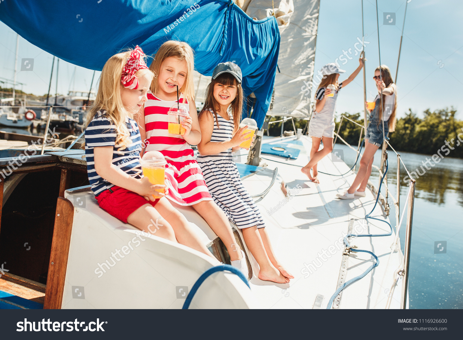 The children on board of sea yacht drinking orange juice. The teen or child girls against blue sky outdoor. Colorful clothes. Kids fashion, sunny summer, river and holidays concepts. #1116926600