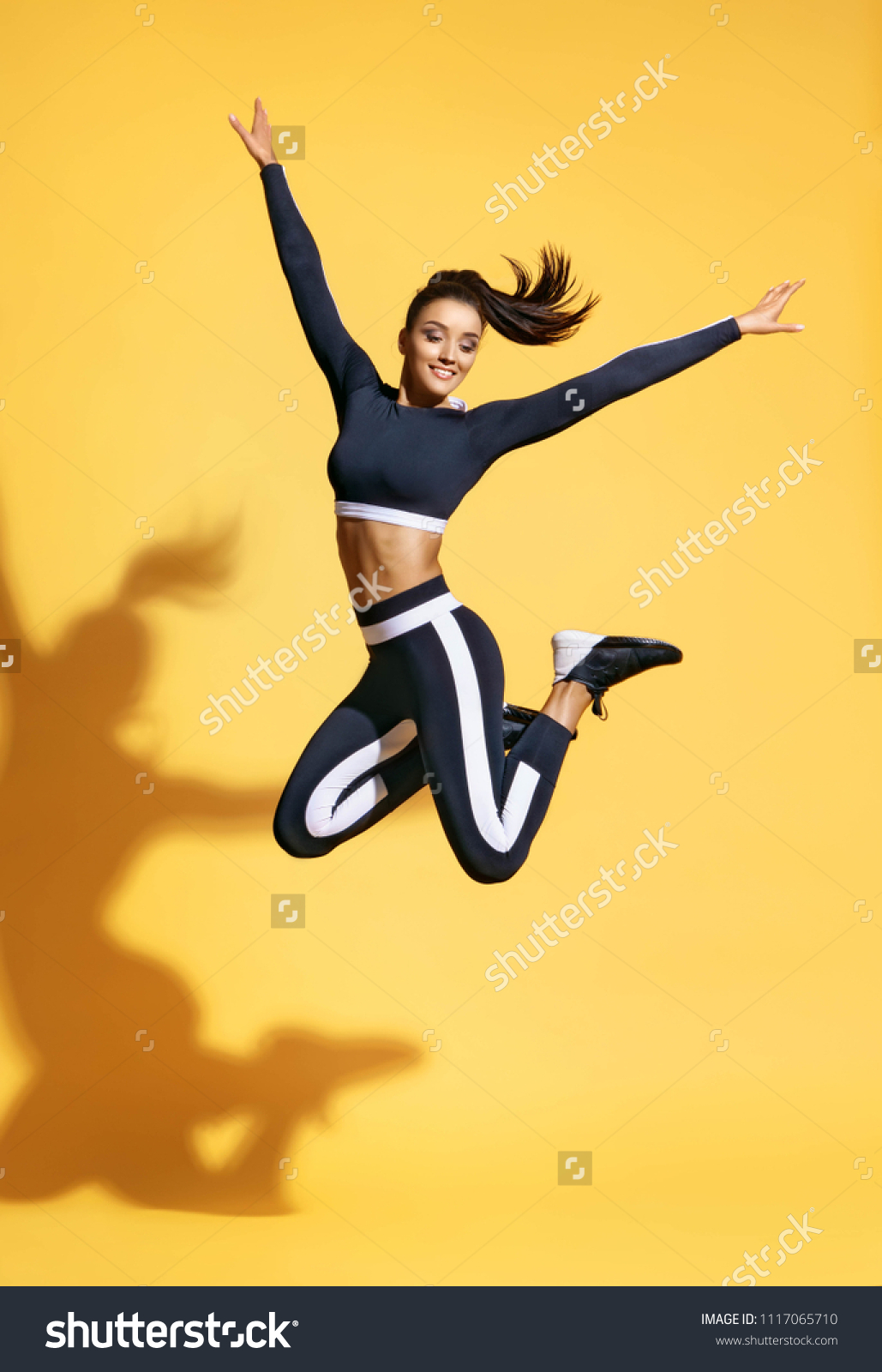 Sporty smiling woman jumping up in silhouette on yellow background. Dynamic movement. Sport and healthy lifestyle #1117065710