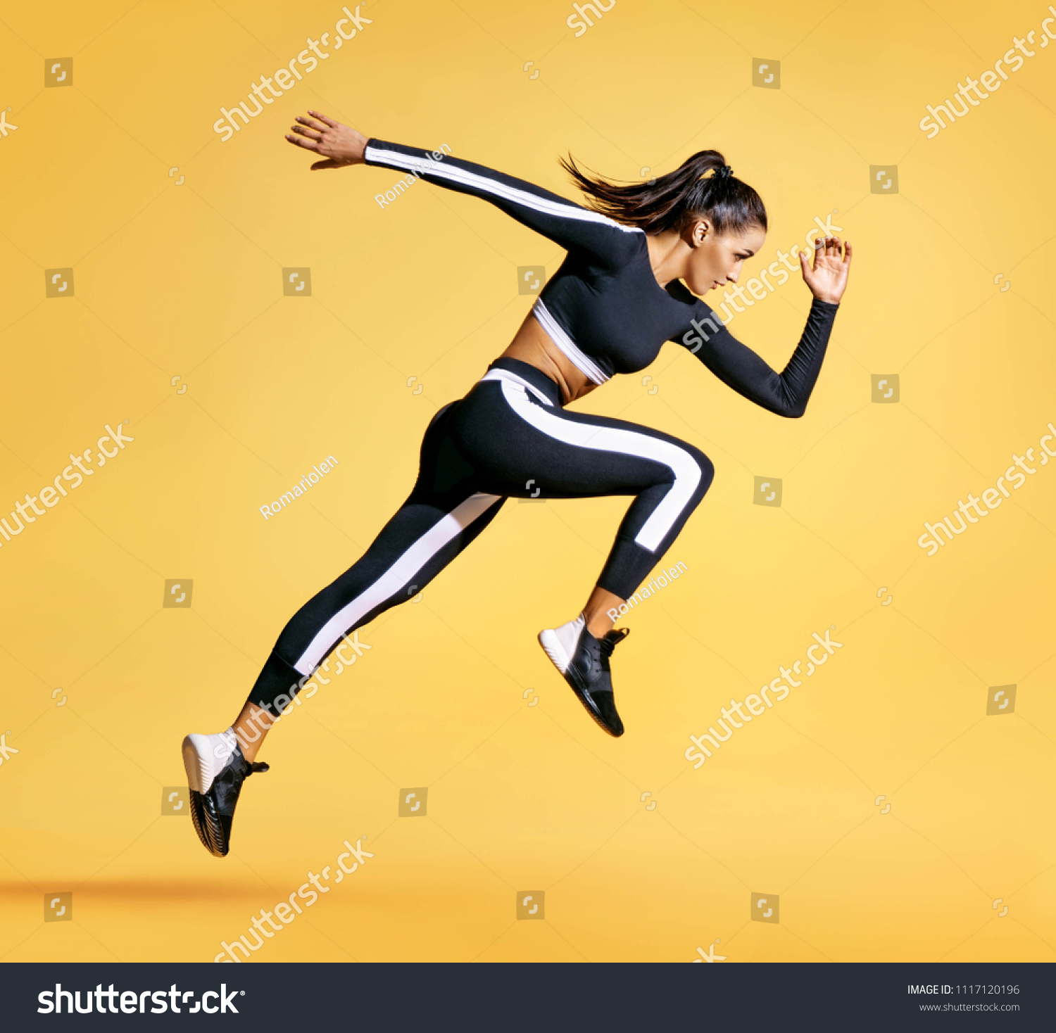 Sporty woman runner in silhouette on yellow background. Photo of attractive woman in fashionable sportswear. Dynamic movement. Side view. Sport and healthy lifestyle #1117120196