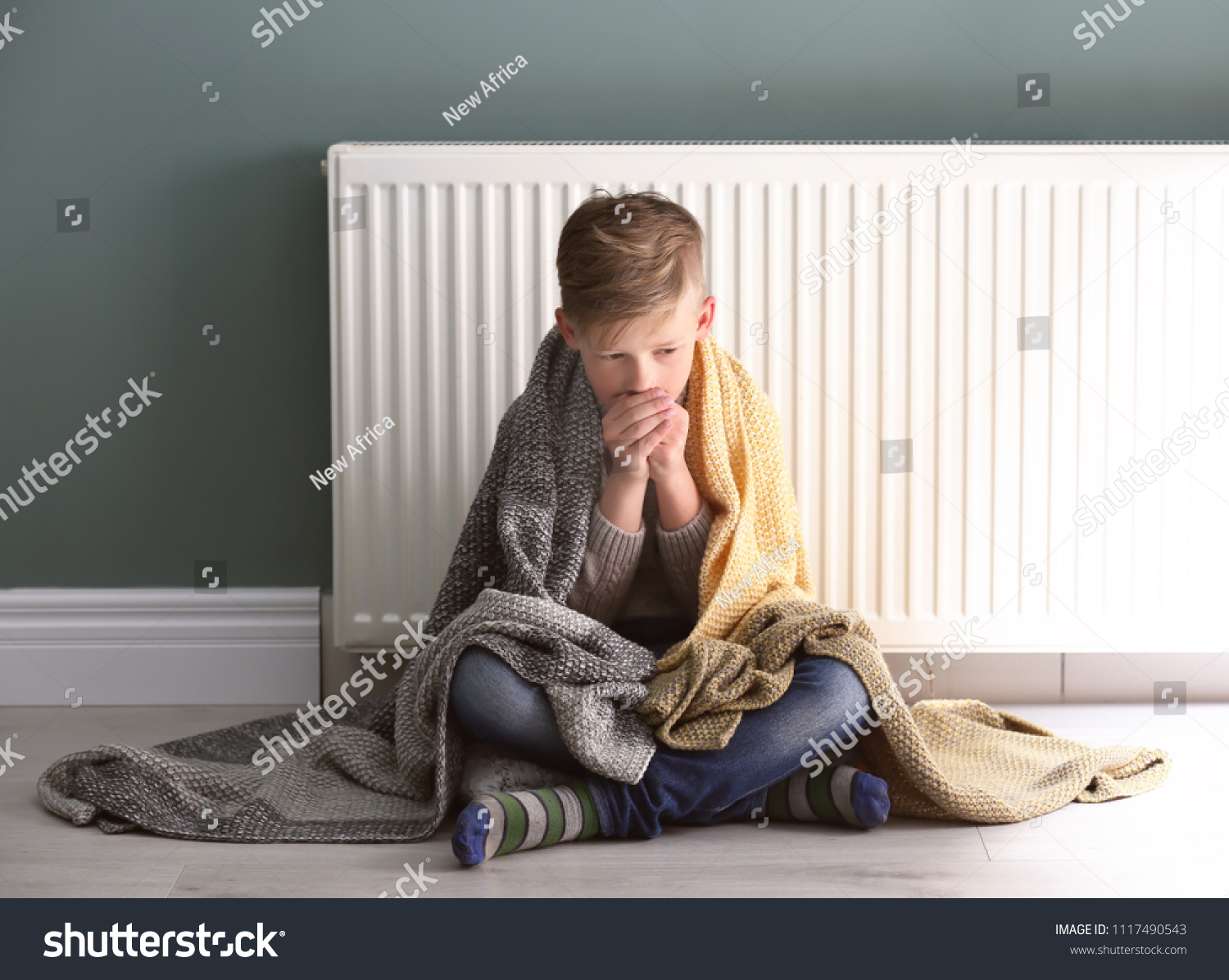 Sad little boy suffering from cold on floor near radiator #1117490543