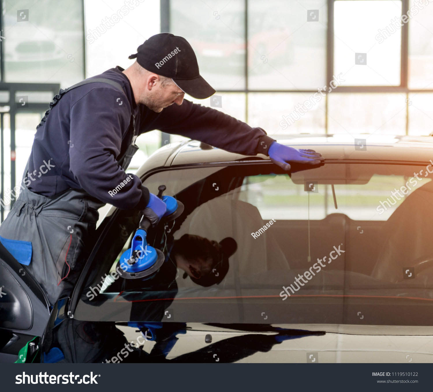 Automobile special workers replacing windscreen or windshield of a car in auto service station garage. Background #1119510122