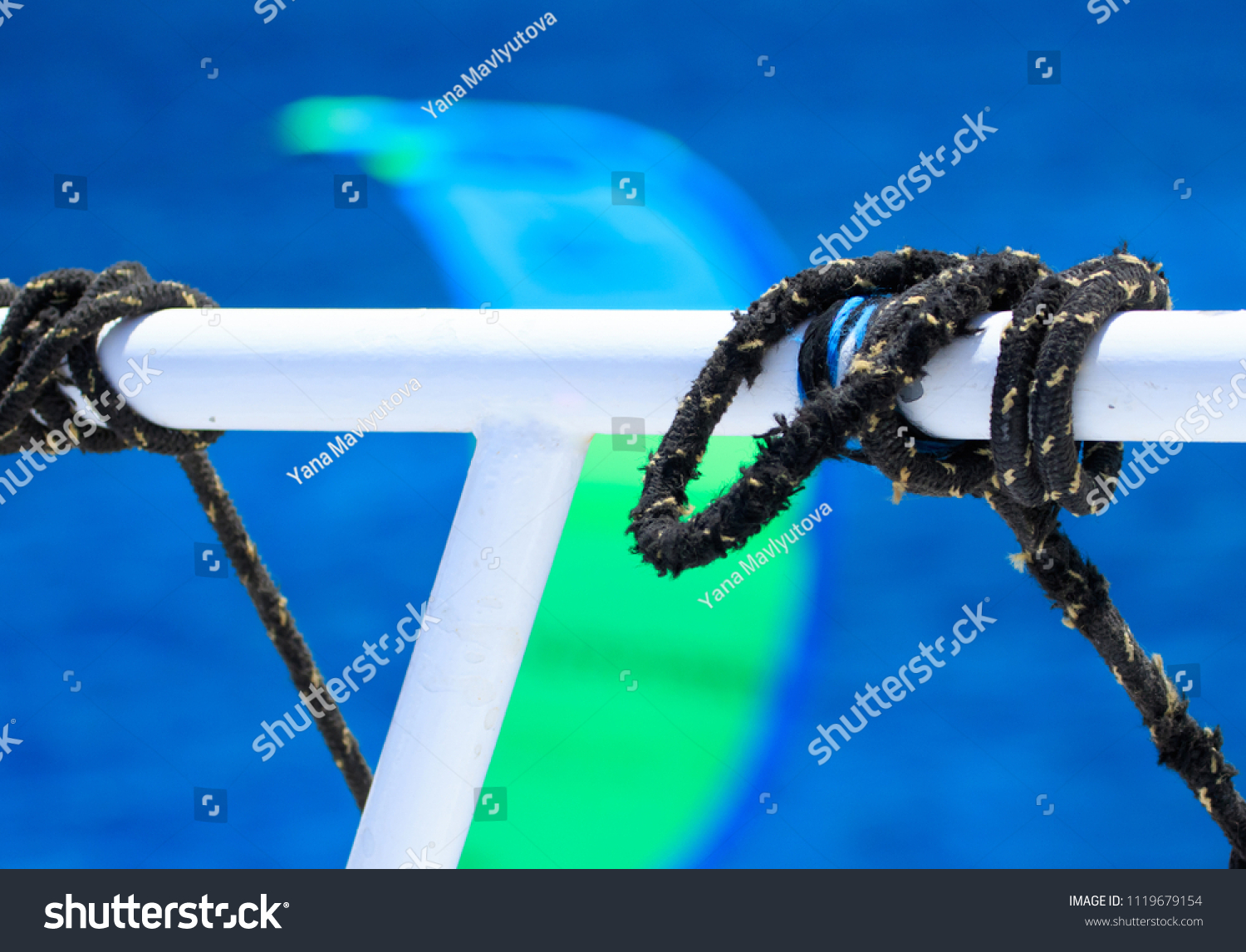 Black sailing ropes crossing in tie knots around boat white tube on blurred bokeh deep blue sea water background, picturesques abstraction eye catching picture for designs prome sail trips tourism #1119679154