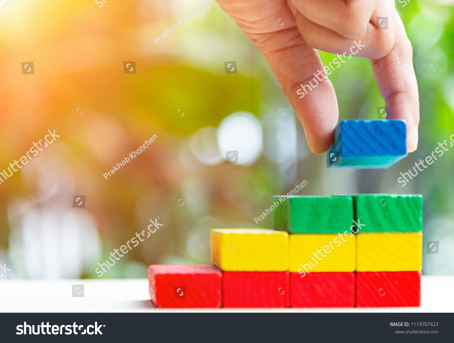 Concepts of building a staircase and step up of wooden pegs for another entrepreneur to climb up the ladder of success.Two finger hold blue block wood last piece for close project. #1119707423
