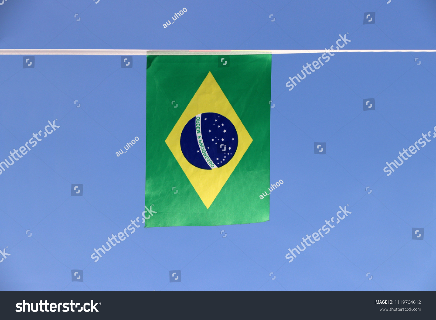 Mini fabric rail flag of Brazil, a blue disc depicting a starry sky with the national motto Order and Progress, within a yellow rhombus, on a green field. It hanging on the rope cloth on blue sky. #1119764612