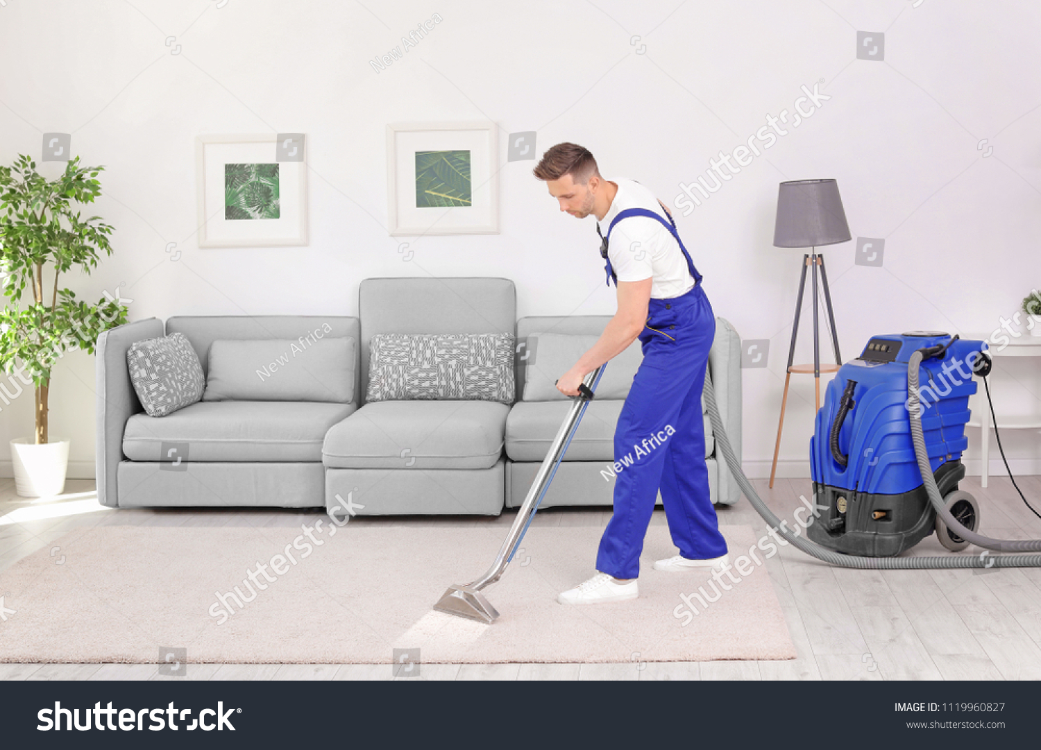 Male worker removing dirt from carpet with professional vacuum cleaner indoors #1119960827