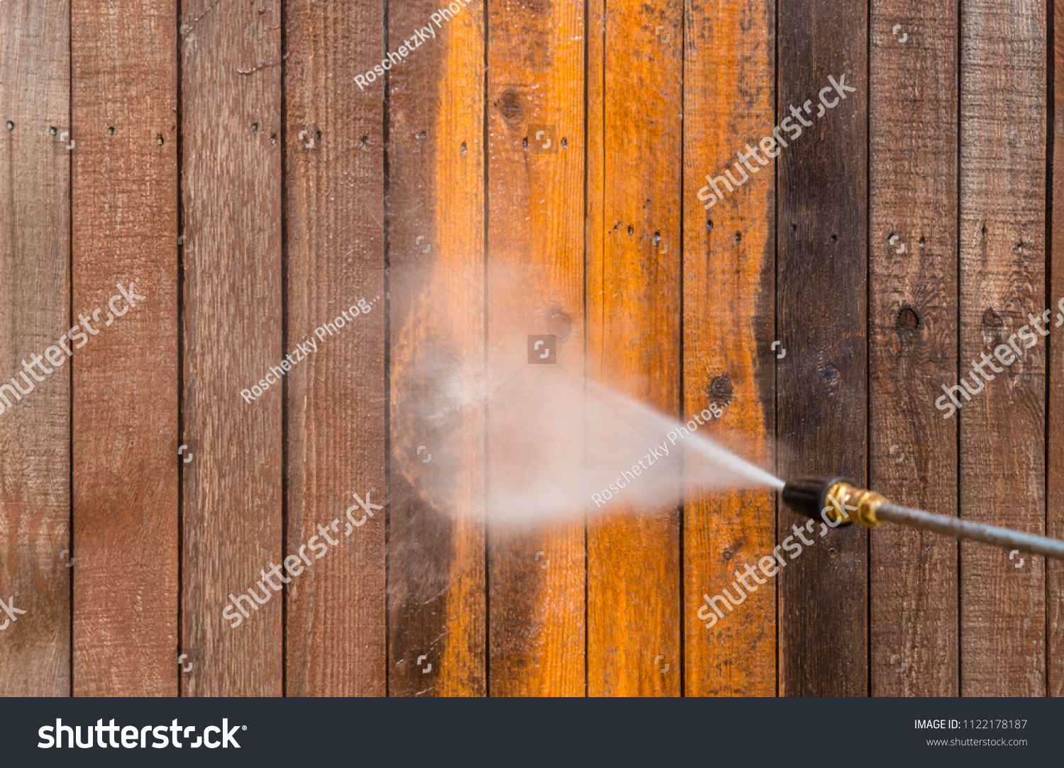 High pressure power washer spraying and cleaning wooden fence. Make old turn new. Dirty fence turned brand new again. Brown dirty grimy wood turned into golden oak again #1122178187