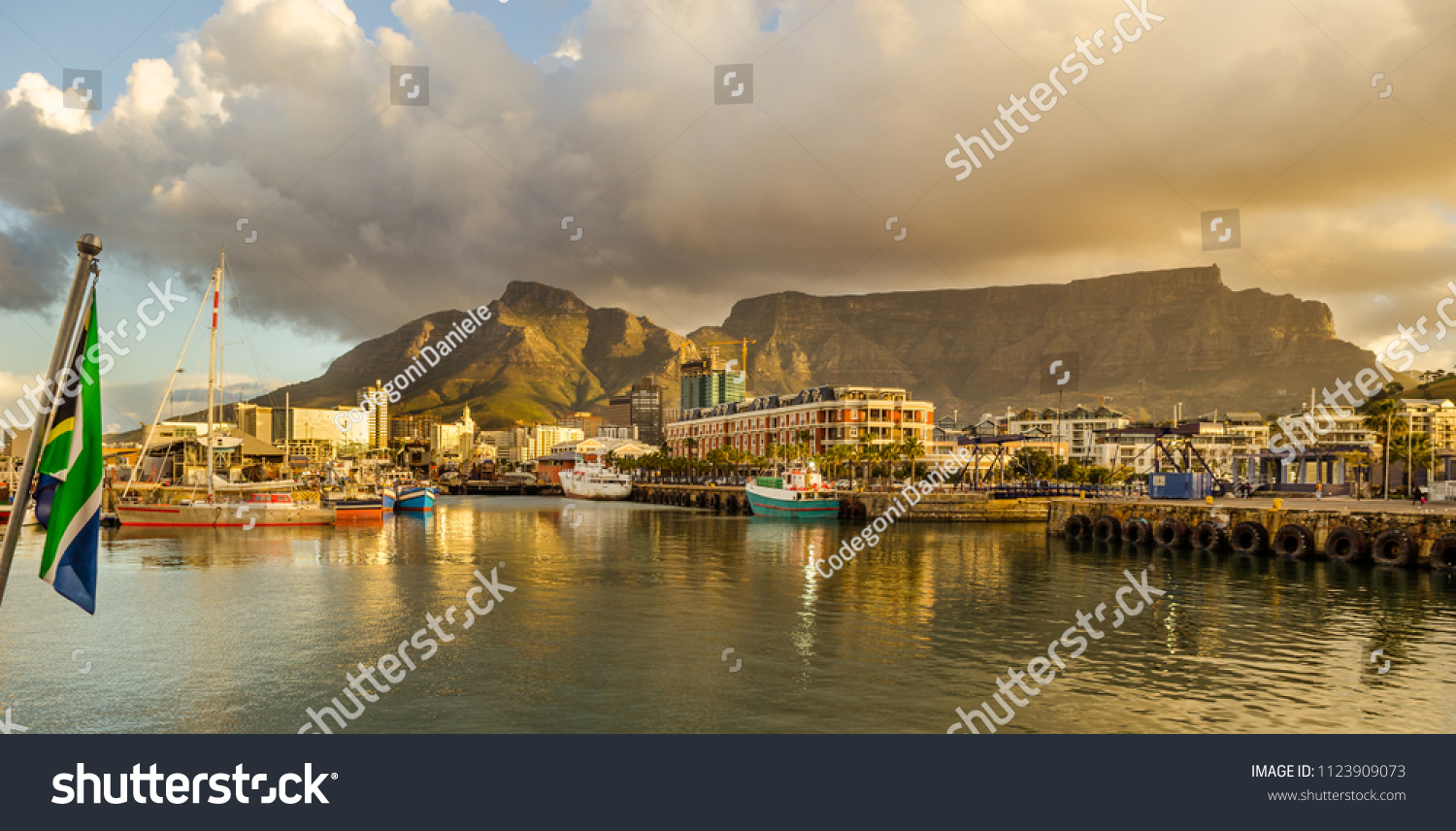 Cape Town harbor, Victoria and Alfred Waterfront at sunset with south african flag. Table mountain in background, South Africa beautiful destination #1123909073