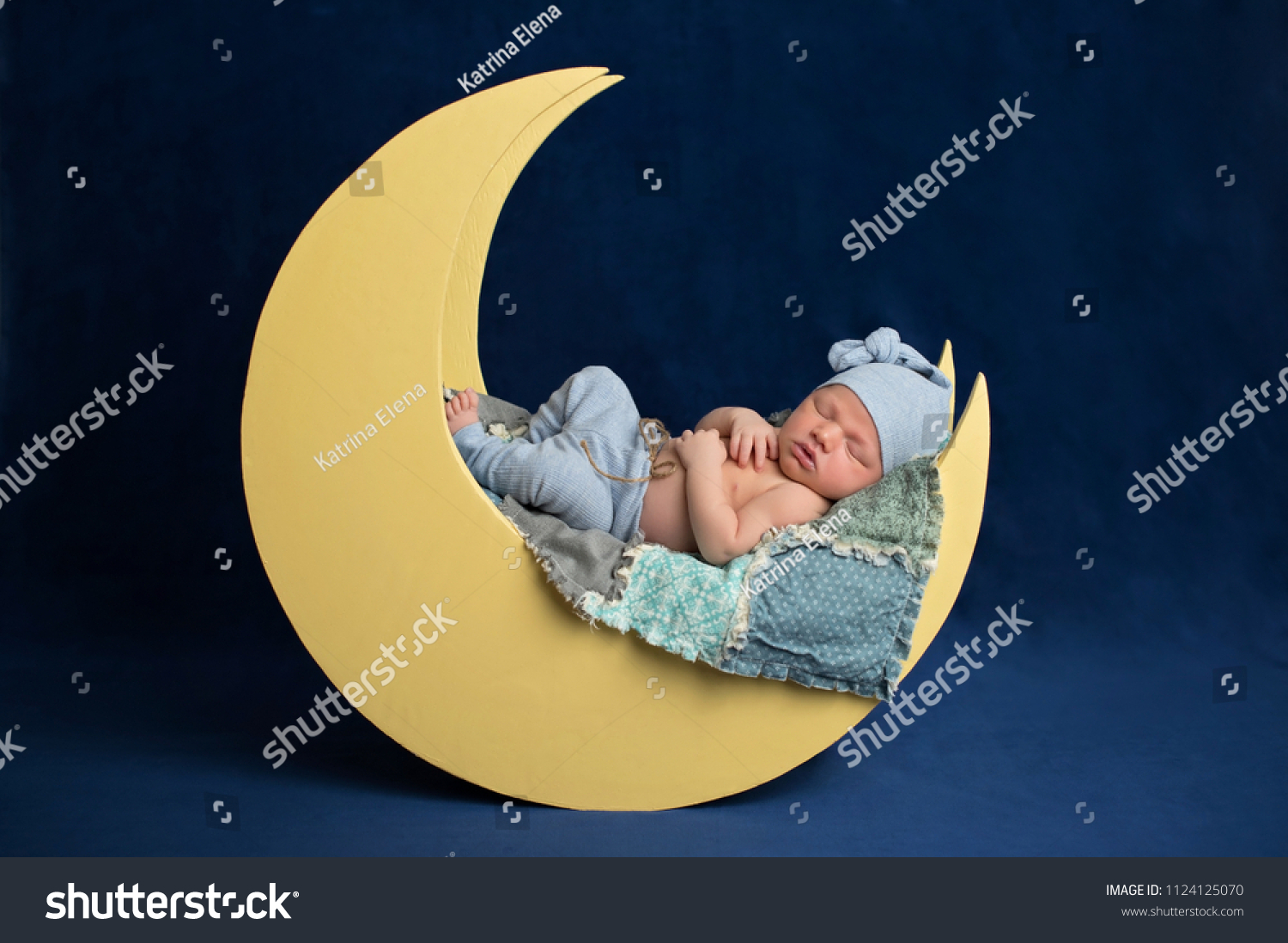 Studio portrait of a ten day old newborn baby boy wearing pajama bottoms and a sleeping cap. He is sleeping on a moon shaped posing prop. #1124125070