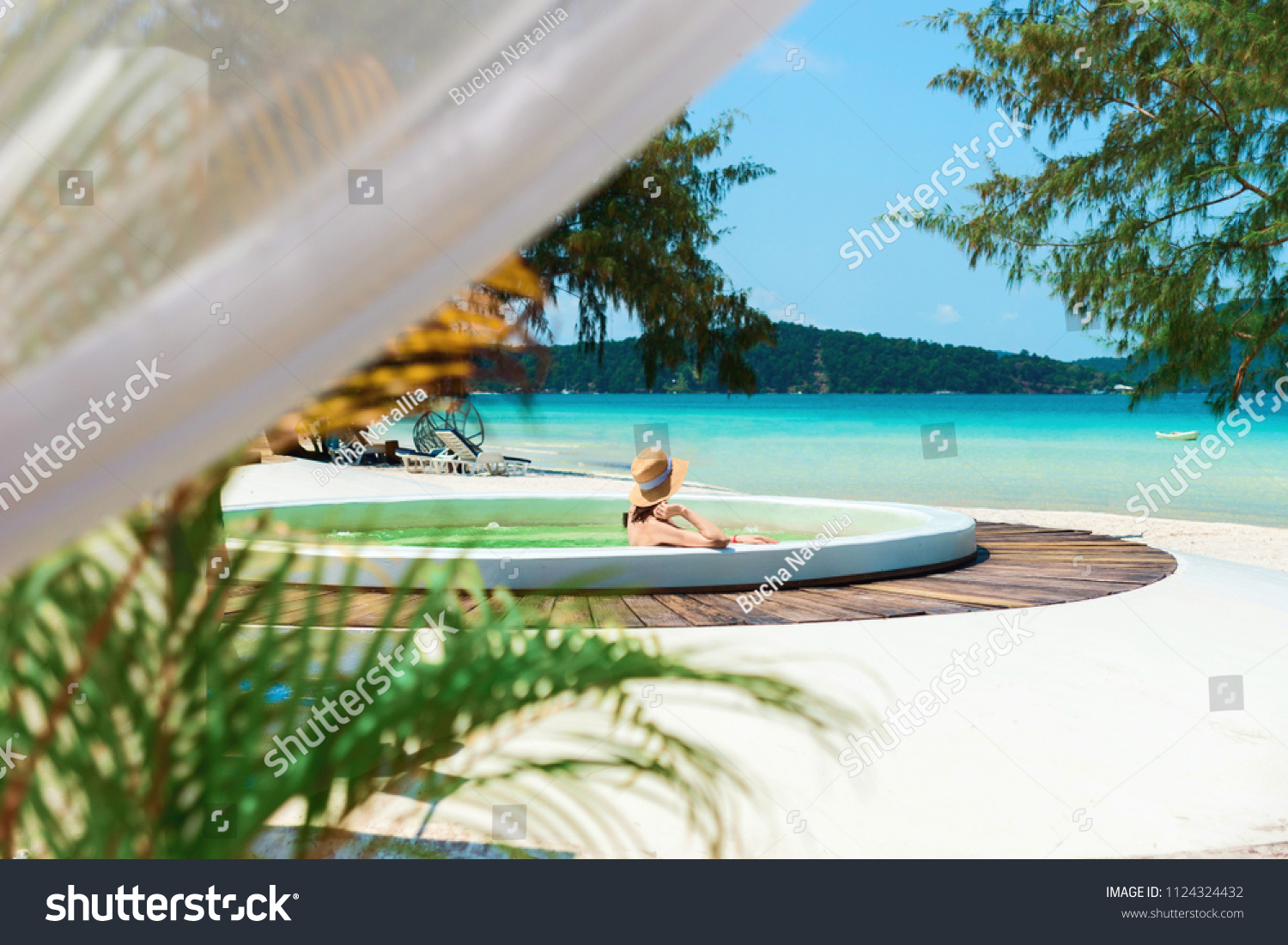 A young woman in a jacuzzi admires a beautiful view of the sea and a white sandy beach, Cambodia, Ko Rong Island.A girl rests in a jacuzzi in the fresh air against the turquoise sea. #1124324432