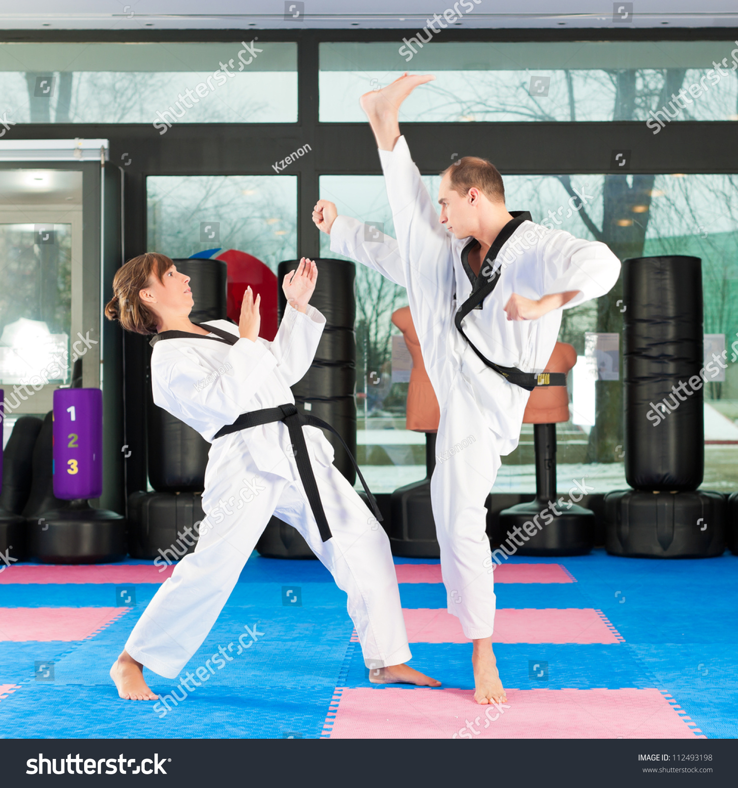 People in a gym in martial arts training exercising Taekwondo, both have a black belt #112493198