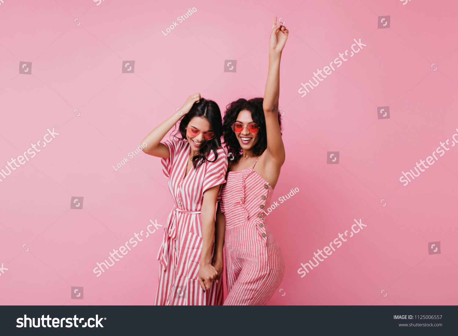 Sensual african lady having fun with her best friend. Indoor photo of adorable girls in pink clothes standing on light background. #1125006557