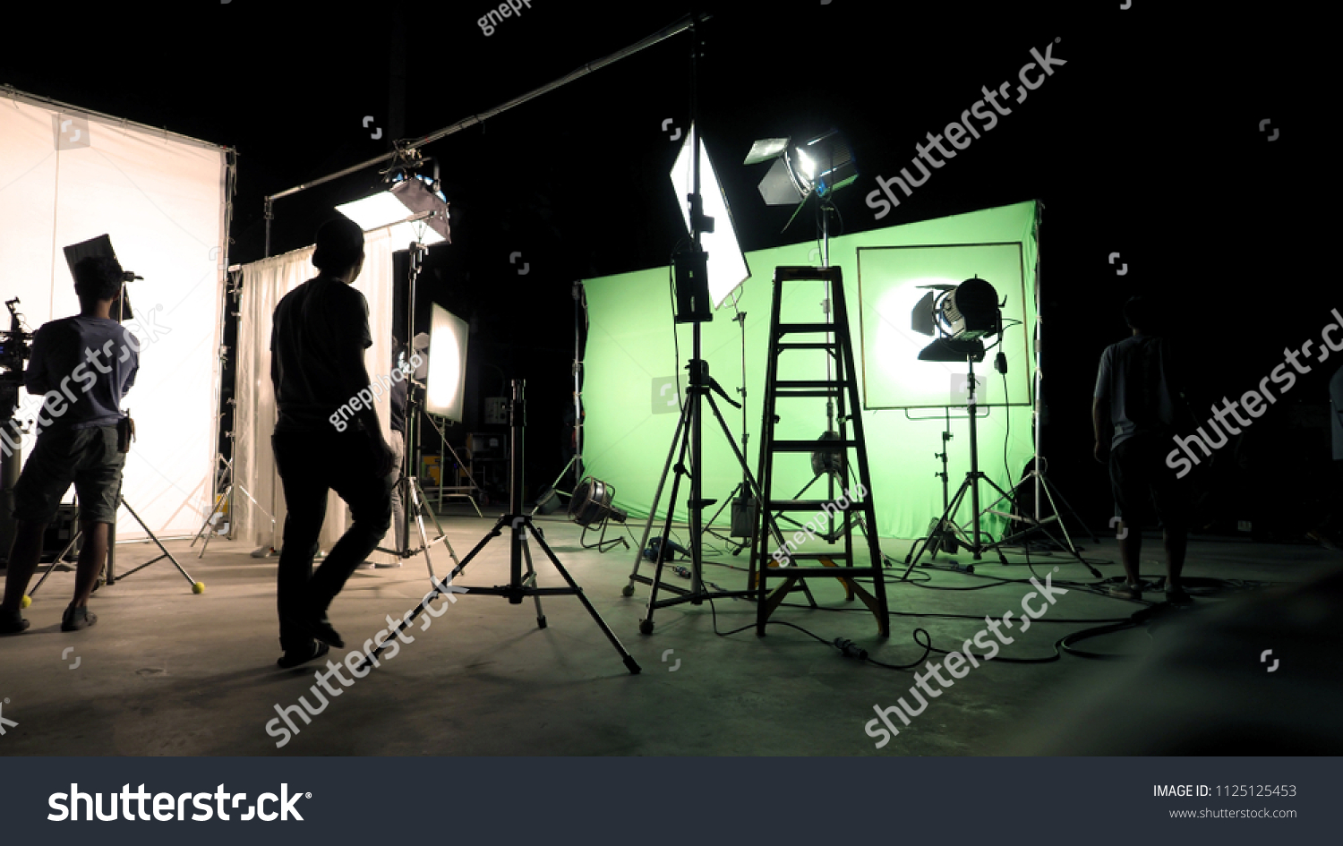 Behind the scenes of TV commercial movie film or video shooting production which crew team and camera man setting up green screen for chroma key technique in big studio. #1125125453