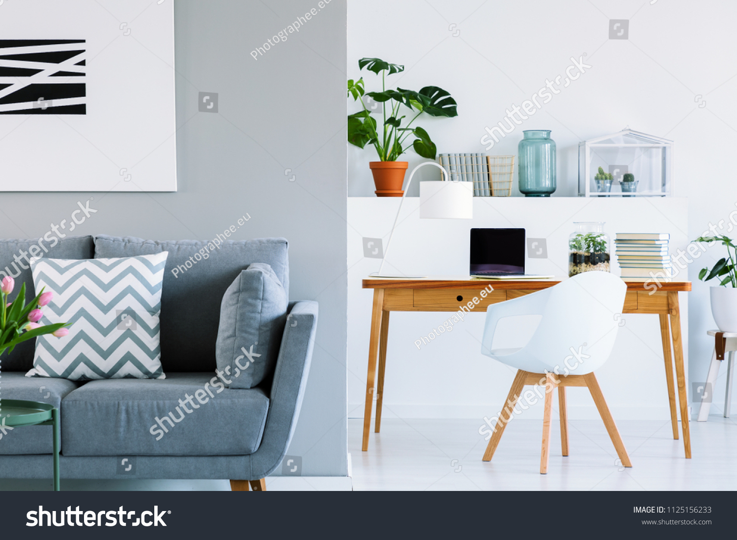 Patterned cushion on grey sofa in scandinavian home office interior with chair at desk. Real photo #1125156233