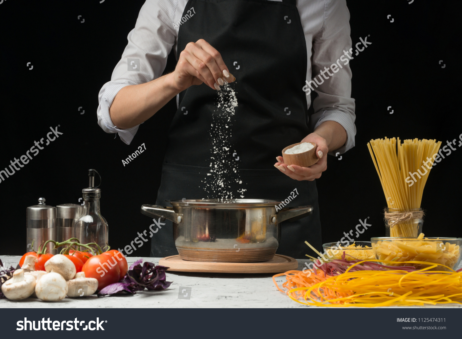 The chef prepares spaghetti and pasta, salt water, against a dark background, the concept of cooking #1125474311