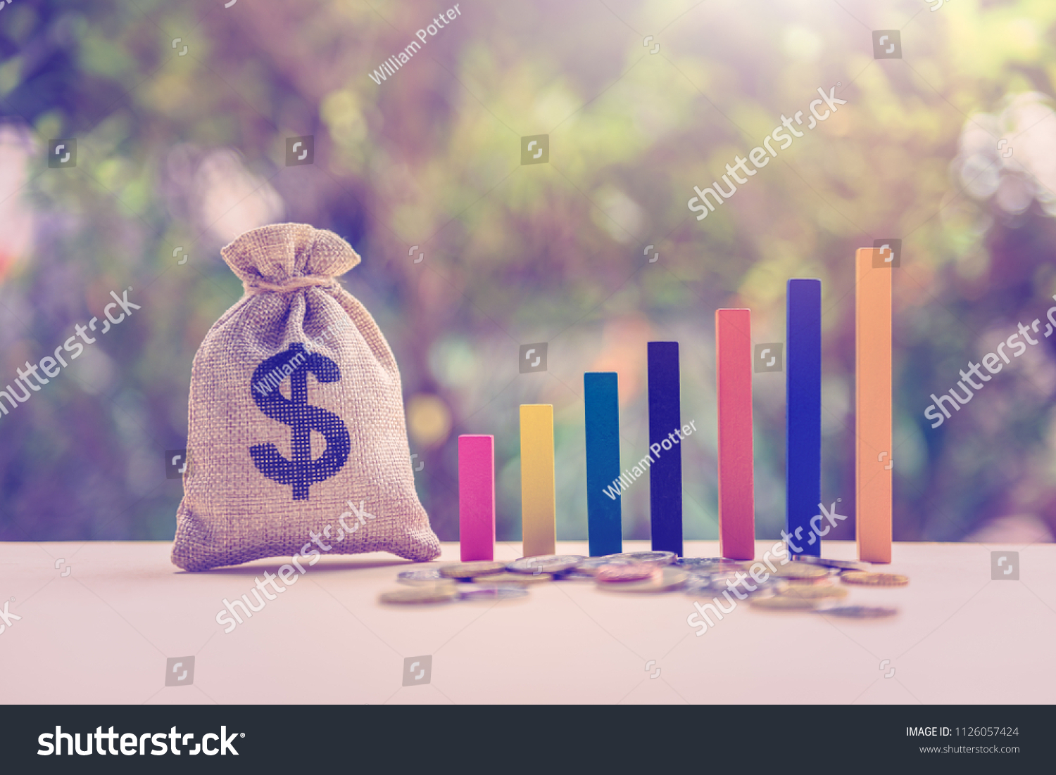 Government budget / public spending concept : Dollar bag, coins, color wood bar graph on a table, depicts the increment in annual financial budget or revenues that government collects from tax payer. #1126057424