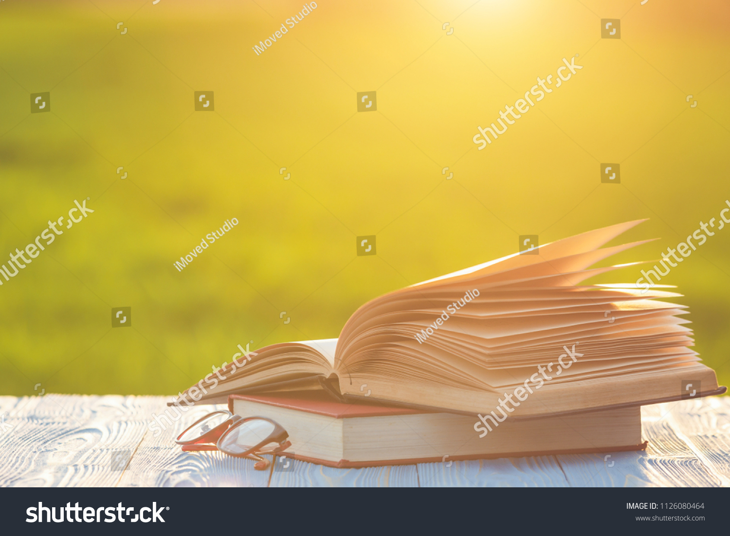 Close up book and eye glasses on wooden table with abstract blur and bokeh in sunrise or sunset time #1126080464