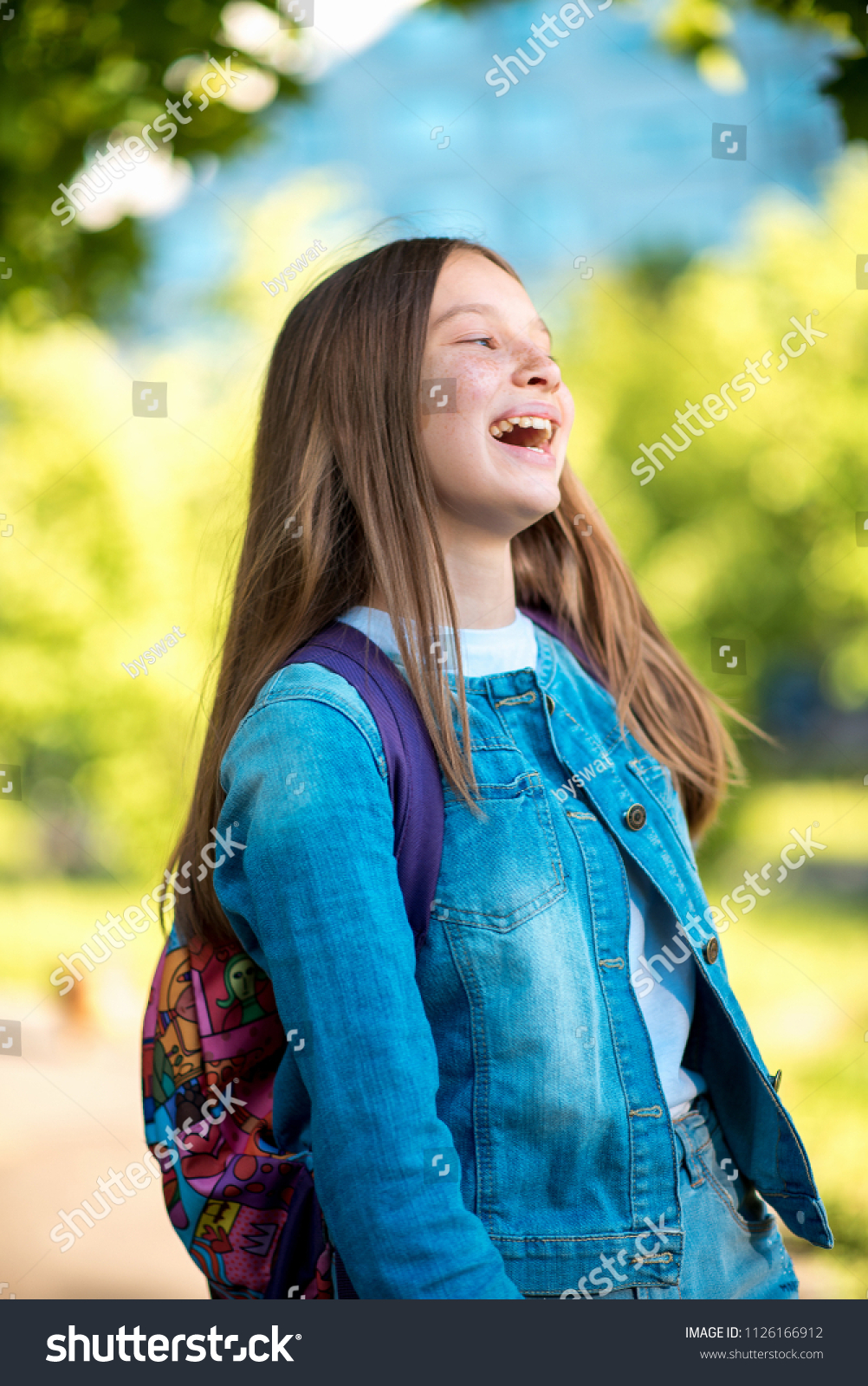 Beautiful schoolgirl girl. Summer in nature. Dressed in jeans clothes behind her backpack. Concept back to school. Emotion of happiness pleasure pleasure, bright children's laughter. #1126166912