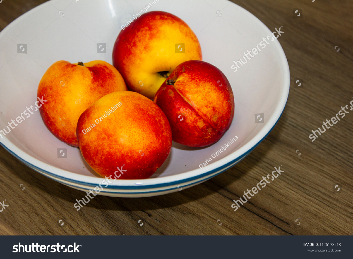 several bright juicy nectarines in the white bowl on wooden table #1126178918