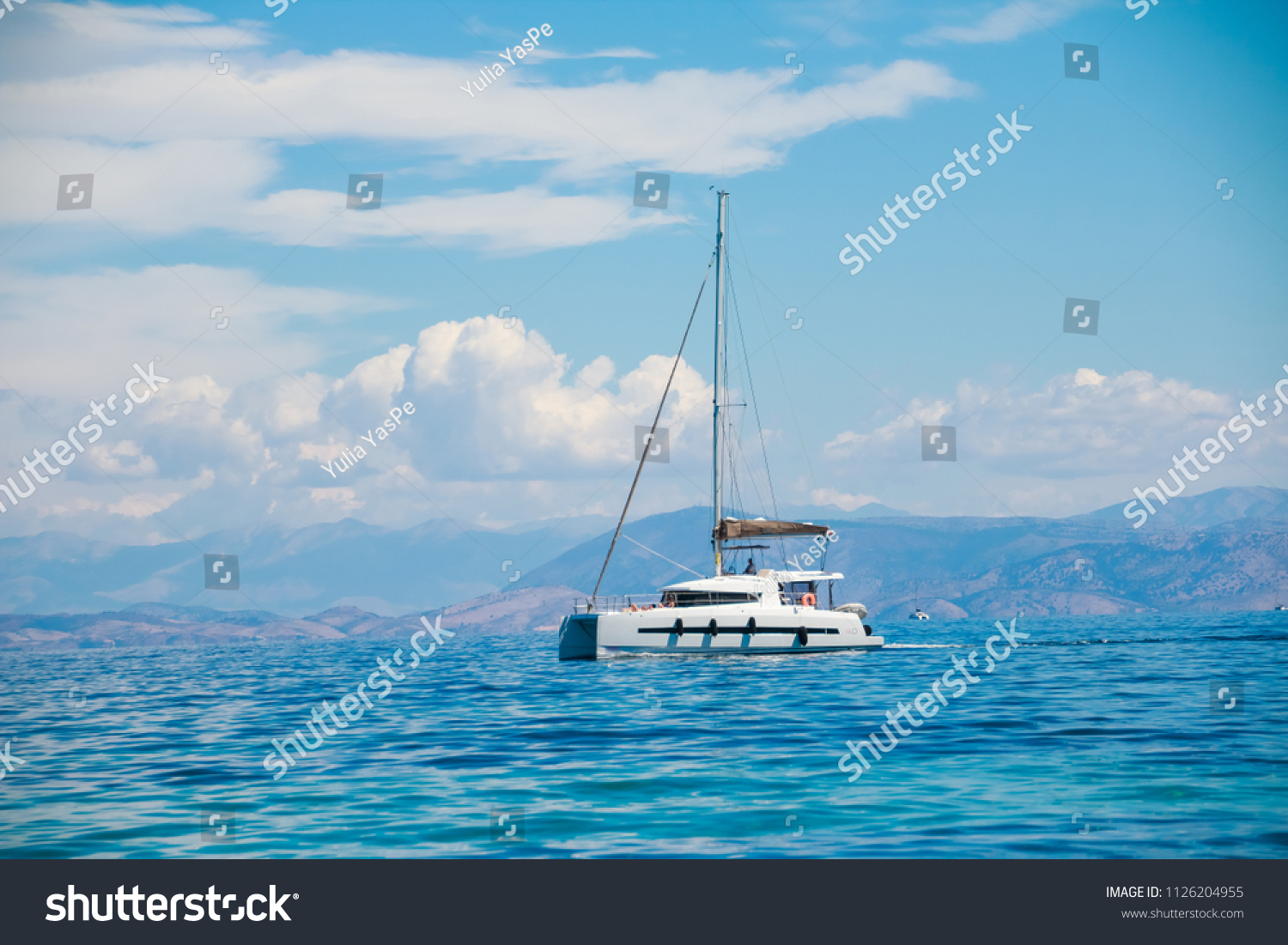 Asingle catamaran in the open sea.Sailboat in the Mediterranean Sea.catamaran sailing boat near coast.catamaran sail boat docked in tropical clear waters.Trendy colors. aqua menthe .Copy space #1126204955