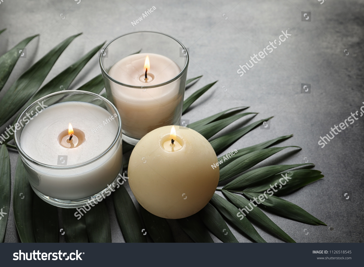 Burning wax candles and tropic leaf on table #1126518545