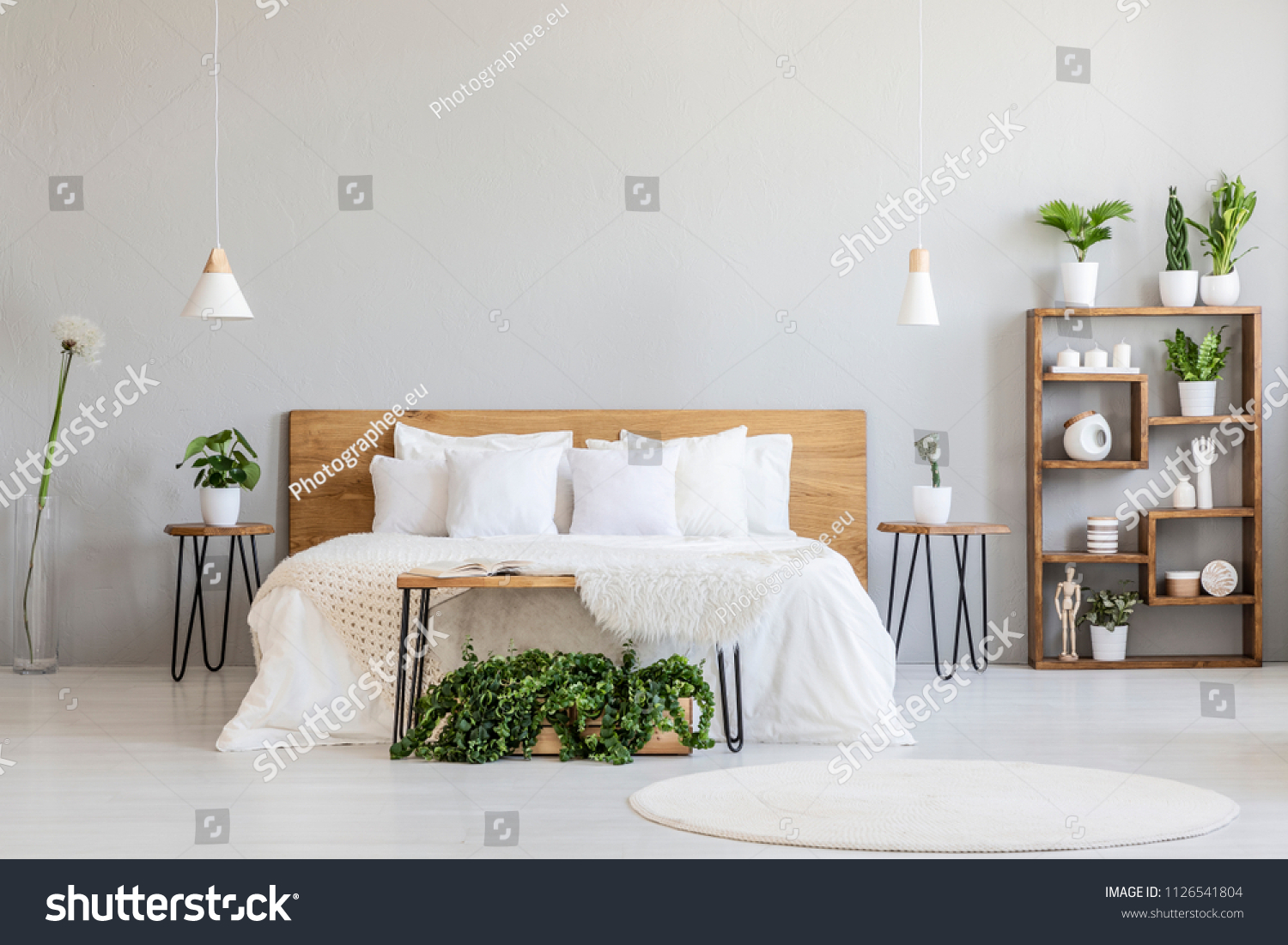 White pillows on wooden bed in minimal bedroom interior with plants and round rug. Real photo #1126541804