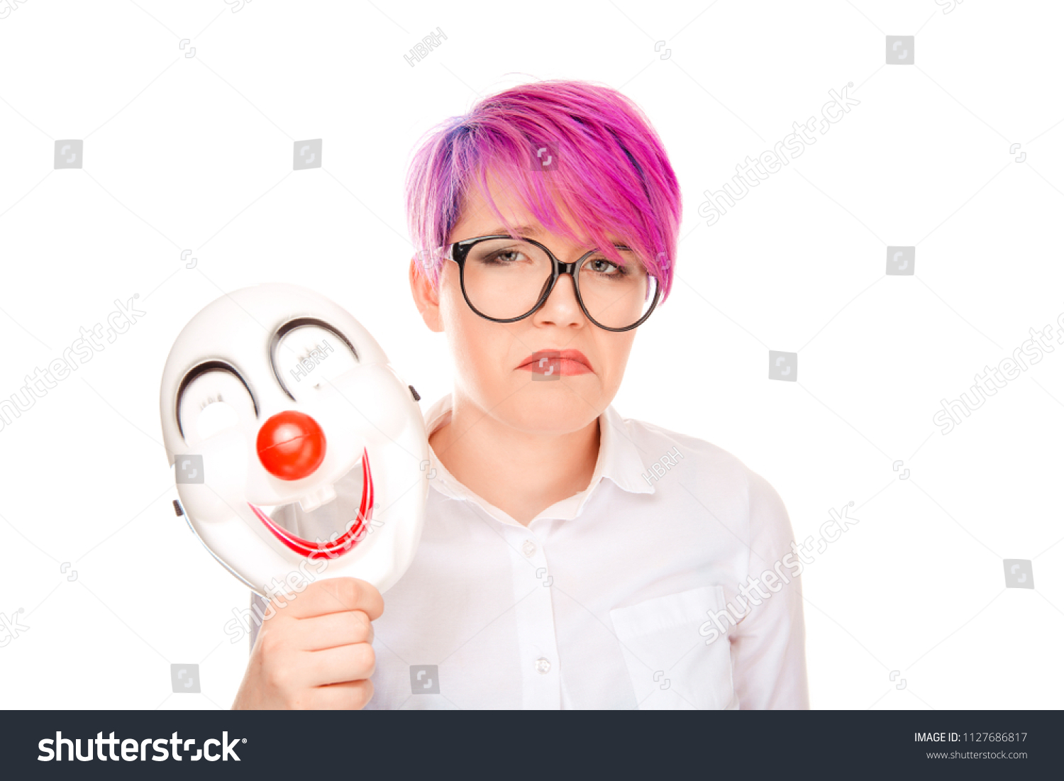 Portrait young upset worried woman with sad expression taking off clown mask expressing cheerfulness happiness isolated on white wall background. Negative facial expressions, human face emotions. #1127686817