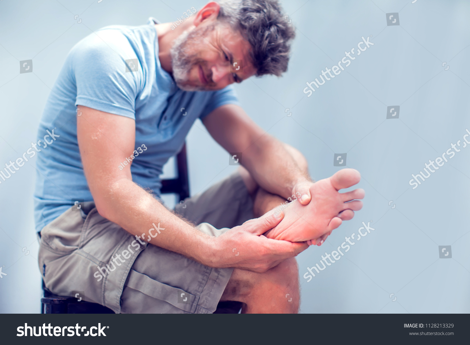 Pain in the foot, man holds hands to his feet, foot massage, cramp, muscular spasm, red accent on the foot, close-up #1128213329