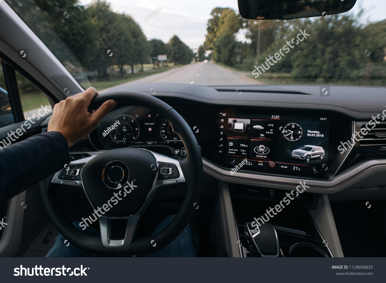 Man is driving a modern SUV car and holds a hand on the steering wheel. Driver goes fast on the city streets, from the first view   #1128690833