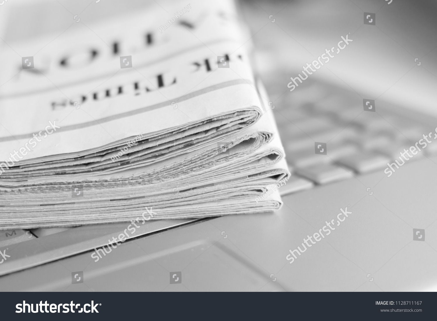 Newspapers and laptop. Pile of daily papers with news on the computer. Pages with headlines, articles folded and stacked on keypad of electronic device. Modern gadget and old journals, focus on paper  #1128711167